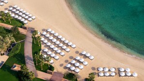 An aerial view of a beach resort with rows of white umbrellas and lounge chairs, a sandy beach, and clear turquoise water. - Rixos Marina Abu Dhabi (Abu Dhabi)