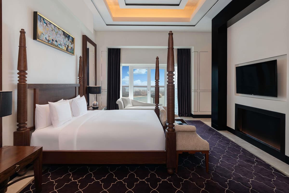A hotel room with a large bed, a TV, a desk, and a view of the city.