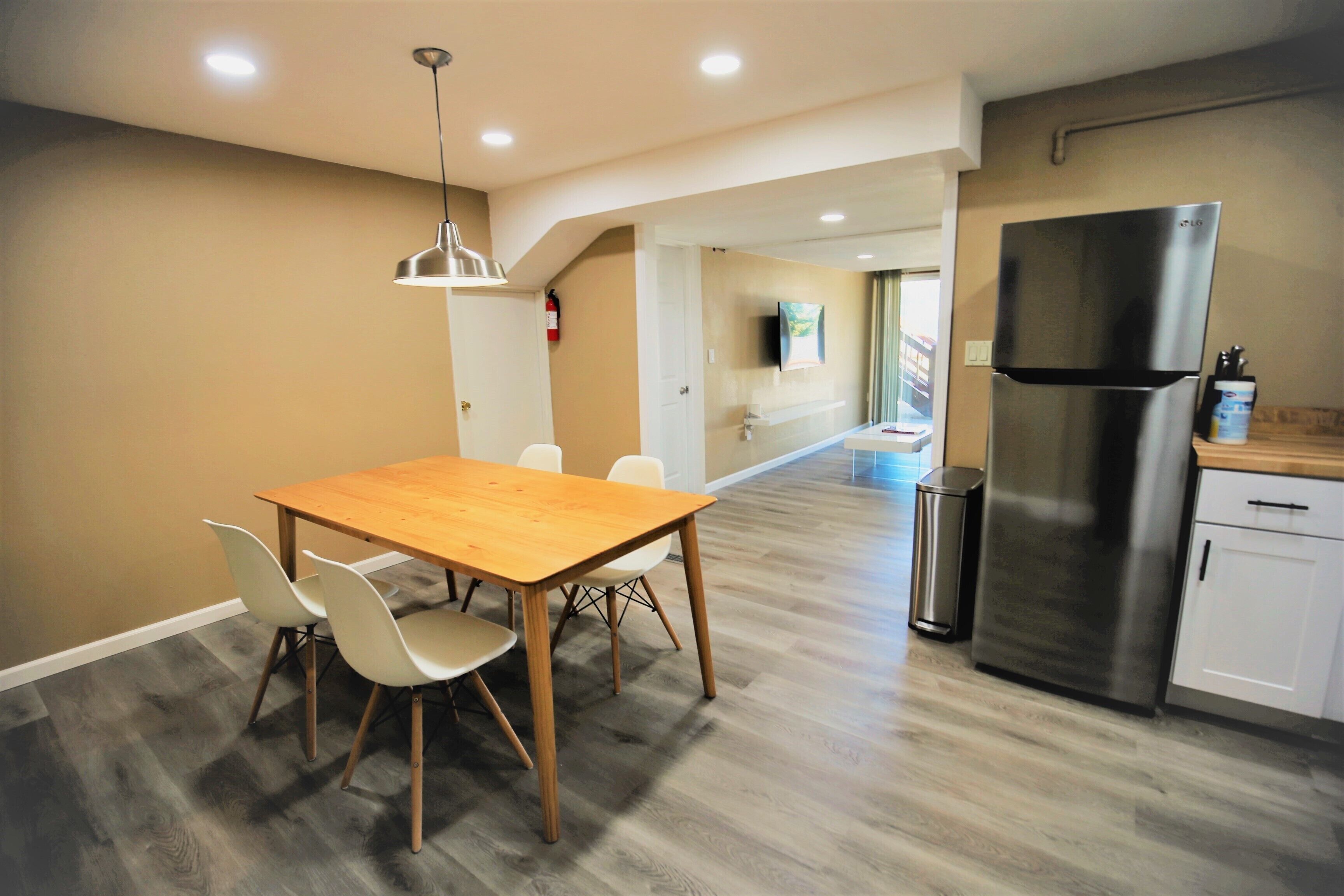 A modern kitchen with a wooden dining table, white chairs, a stainless steel refrigerator, and a built-in oven.