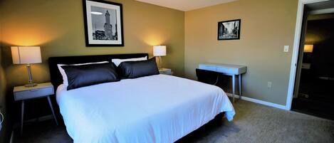A hotel room with a large bed, two bedside tables with lamps, a small desk, and two framed pictures on the walls.