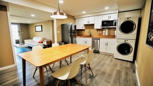 A modern kitchen with a wooden table and chairs, a refrigerator, microwave, oven, and stacked washing machines.