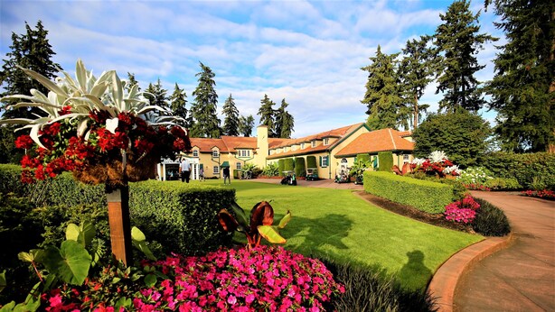 A well-maintained garden with vibrant flowers and a neatly trimmed lawn in front of a large house with a tiled roof.