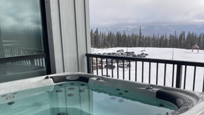 Ein Whirlpool mit Glasverkleidung, Blick auf eine verschneite Landschaft und eine Holzterrasse.
