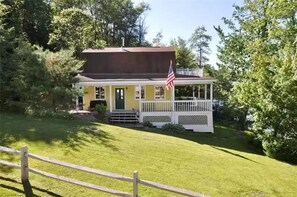 Ein gelbes Haus mit Veranda, einer amerikanischen Flagge und einem umzäunten Garten.