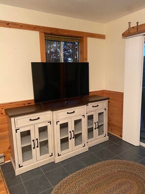 Ein Zimmer mit Fernseher auf einer Holzkabine, einem Fenster mit Blick auf Bäume und einem gemusterten Teppichboden.