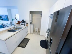 Una cocina compacta con armarios blancos, un refrigerador de acero inoxidable, un microondas y un lavamanos.