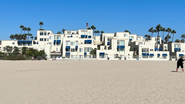Un hotel sulla spiaggia con diversi edifici, palme e un cielo azzurro limpido.