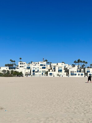 A beachfront hotel with multiple buildings, palm trees, and a clear blue sky. - Pearl Beach Condo - 3 feet from the sand! (Huntington Beach)