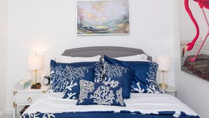 A bedroom with a bed, pillows, a nightstand, a lamp, and a painting on the wall. - Firefly Cottage at the Cape, Hot Tub, Community beach, Boat Show, USNA Football. (Annapolis)