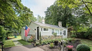 A single-story house with a stone chimney, a front porch, and a well-maintained garden with various plants and flowers. - Firefly Cottage at the Cape, Hot Tub, Community beach, Boat Show, USNA Football. (Annapolis)