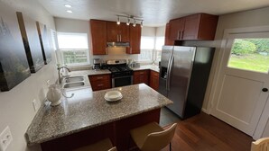 A kitchen with granite countertops, wooden cabinets, stainless steel appliances, and a bar area with stools.