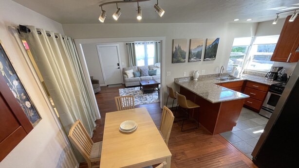 A modern kitchen with a dining area, wooden flooring, and a view of the living room.