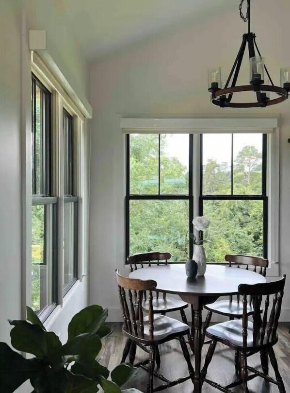 Enjoy meals in this dining area with a round table and six chairs, surrounded by large windows offering a view of the outdoors.