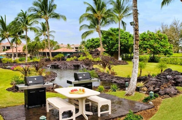 Relax in a serene garden setting with lush greenery, a small pond, and a barbecue area.