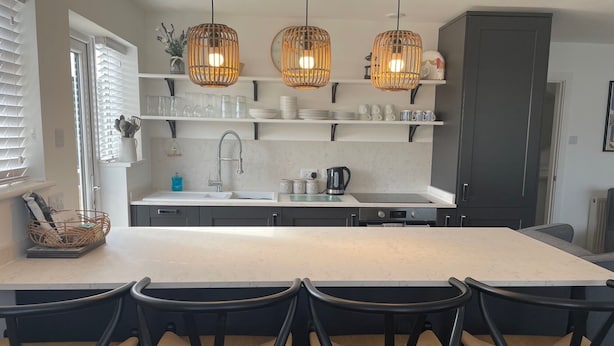 Una cocina moderna con una isla grande, sillas negras y lámparas colgantes de mimbre.