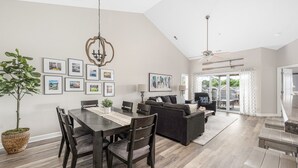 Un vaste espace de vie comprenant une table à manger, des chaises en bois foncé, un canapé et un ventilateur de plafond.