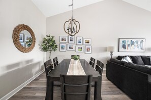 A dining area with a dark wooden table, chairs, a woven mirror, and a chandelier. - Makin’ Memories at Lake Escape, Lake view, Pool - Lake Norman Vacation Rental (Cornelius)