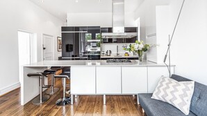 Una cocina moderna con una isla central, taburetes de bar y un sofá gris con un cojín estampado.