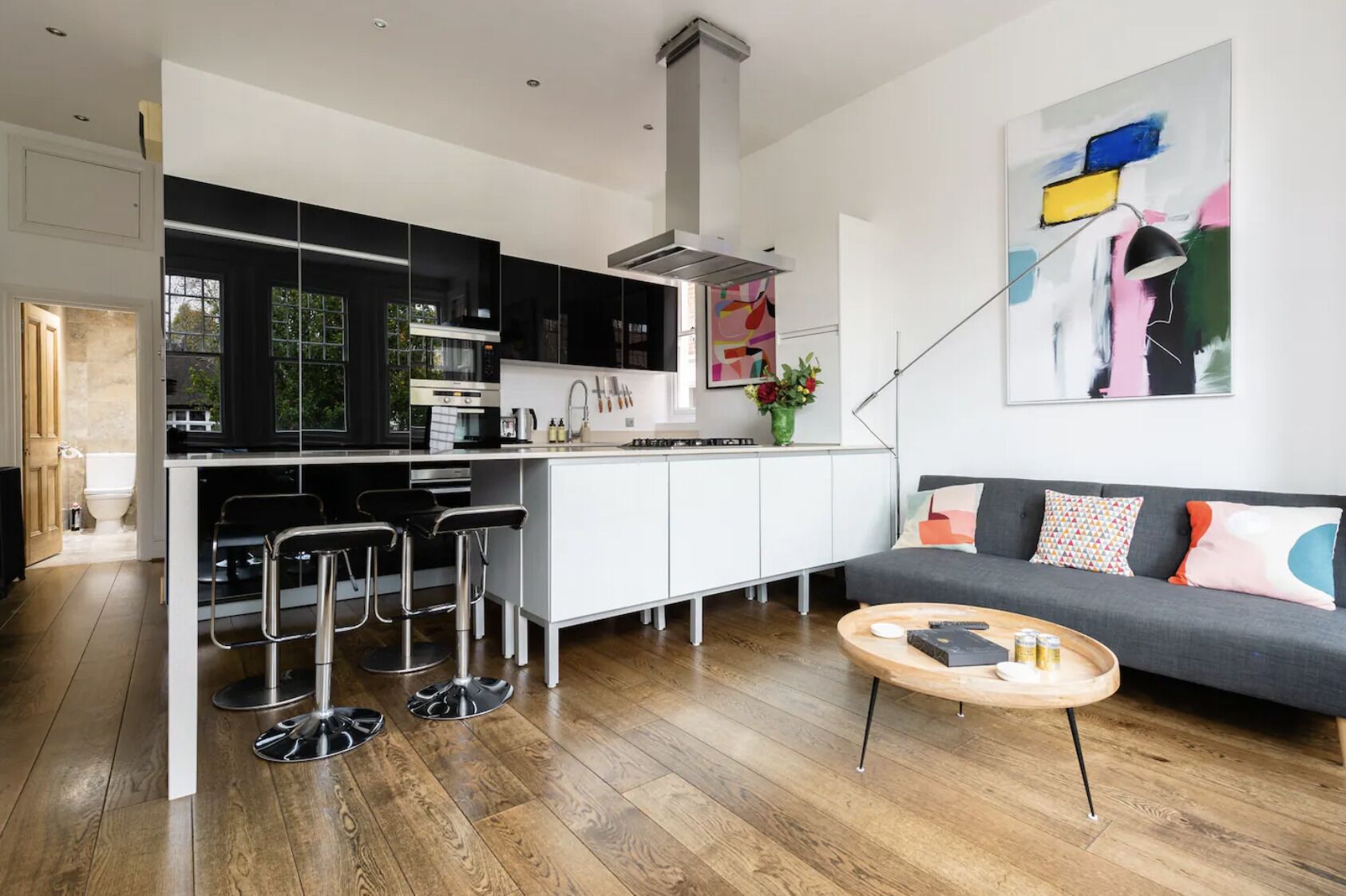 A modern kitchen with a central island, bar stools, and a grey sofa with colorful cushions.