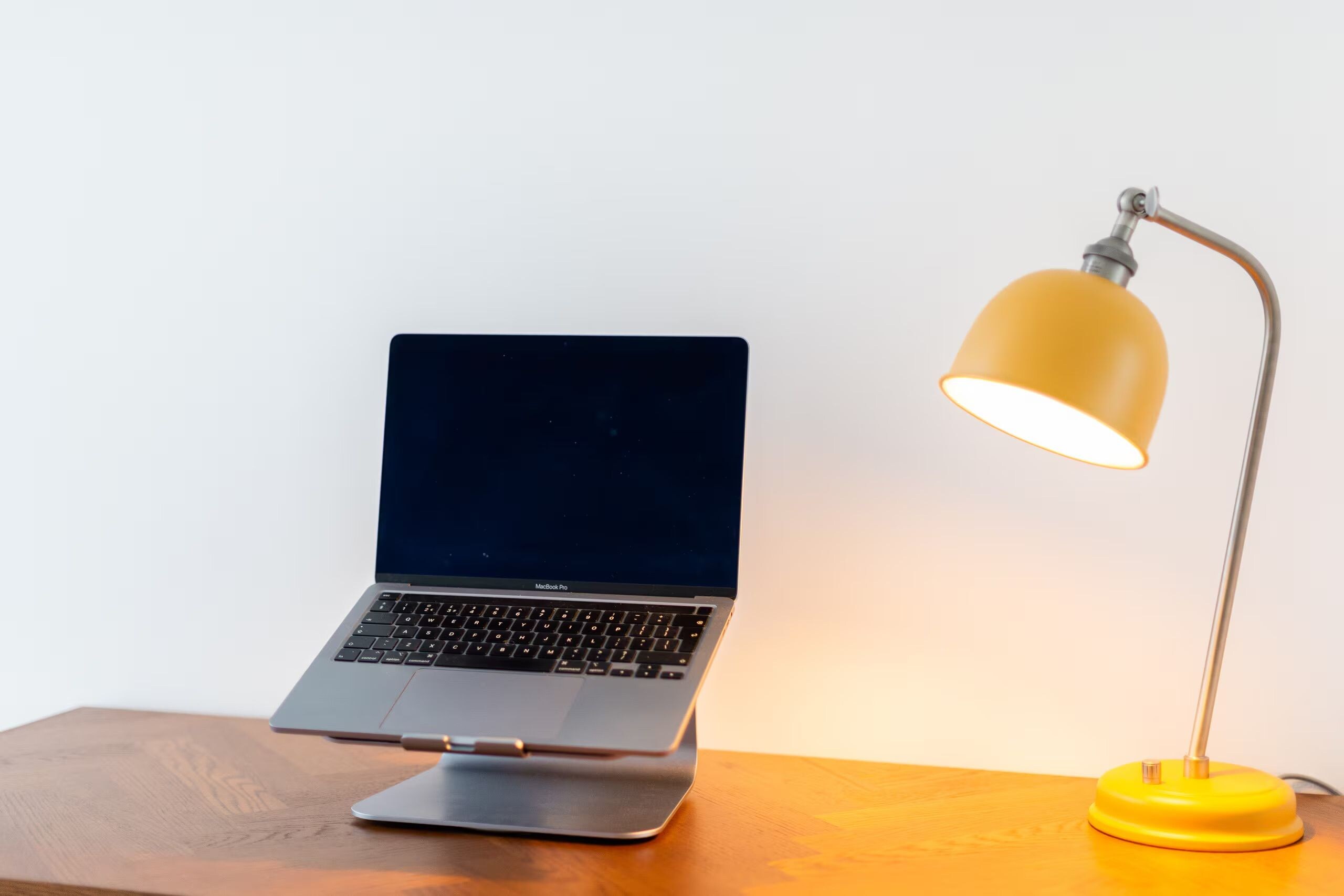 A laptop on a wooden surface with a yellow desk lamp beside it.