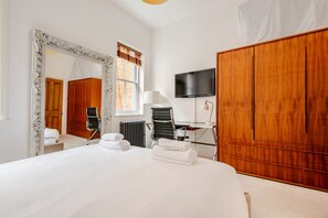 Une chambre d’hôtel avec un grand lit, une armoire en bois, un bureau avec une chaise, une télévision et un miroir.
