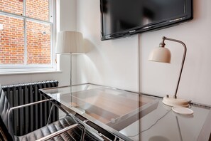 A modern room with a glass-top table, a mounted TV, a lamp, and a radiator. - Luxury Central London 2 x double bed apartment - Hampstead (London)