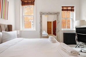 A hotel room with a large bed, a mirror, a radiator, and a view of a brick building. - Luxury Central London 2 x double bed apartment - Hampstead (London)