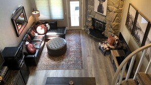 Una sala de estar acogedora con chimenea de piedra, un sofá de cuero negro, un tapiz estampado y una escalera que sube.