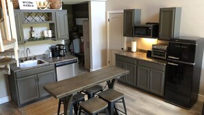 Una cocina con una mesa de madera, taburetes de bar, un refrigerador negro, un microondas y una cafetera.