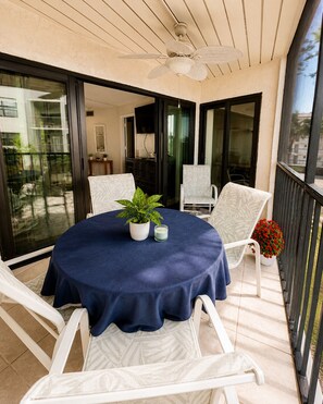 Ein runder Tisch mit blauer Tischdecke, weißen Stühlen, einem Deckenventilator und einem Blumentopf.