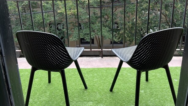 Een balkon met twee stoelen en een tafel, met uitzicht op een gebouw met gebogen ramen en een tuin.