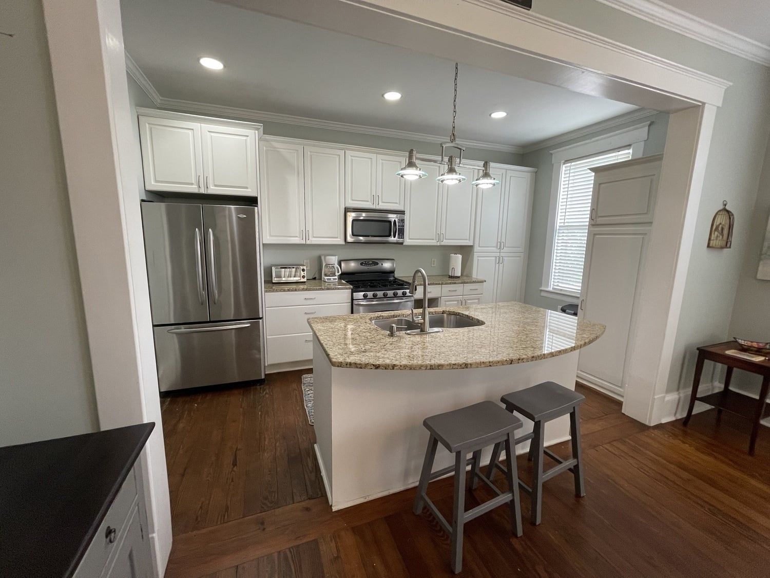 A modern kitchen with white cabinets, stainless steel appliances, a granite countertop, and bar stools.