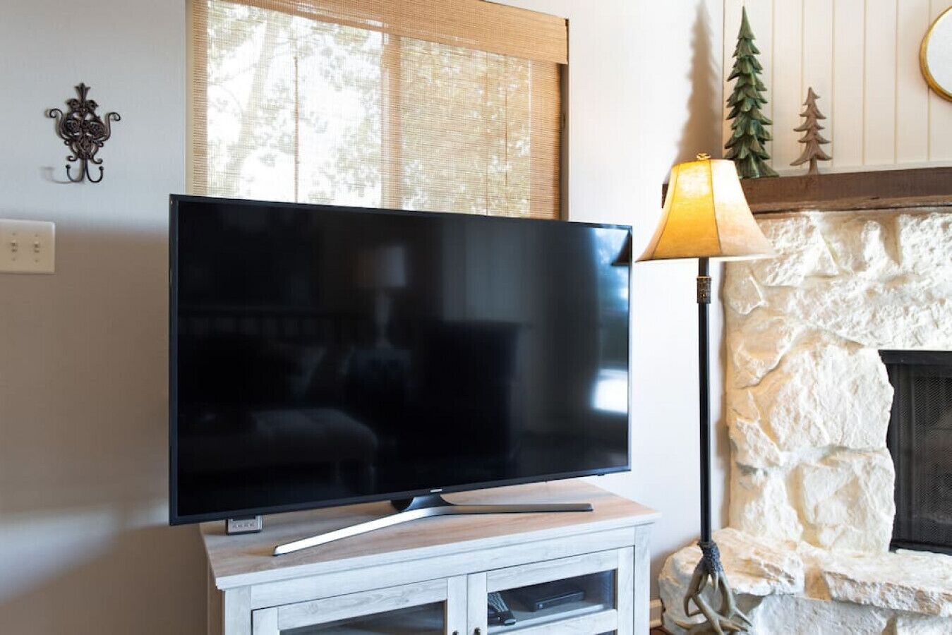 Een flatscreen televisie op een wit kastje, een lamp en een stenen openhaard.