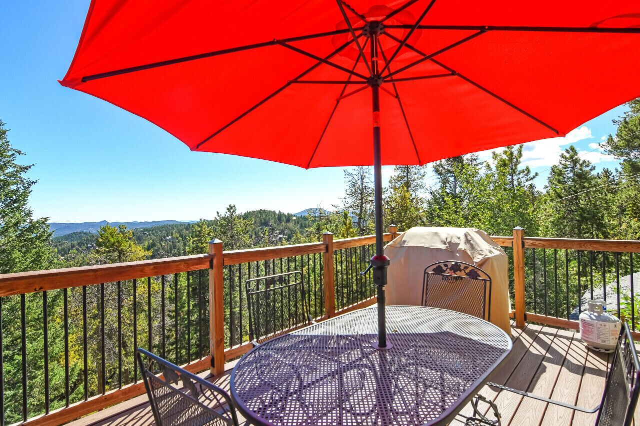 Una terraza con un paraguas rojo, una mesa y sillas.