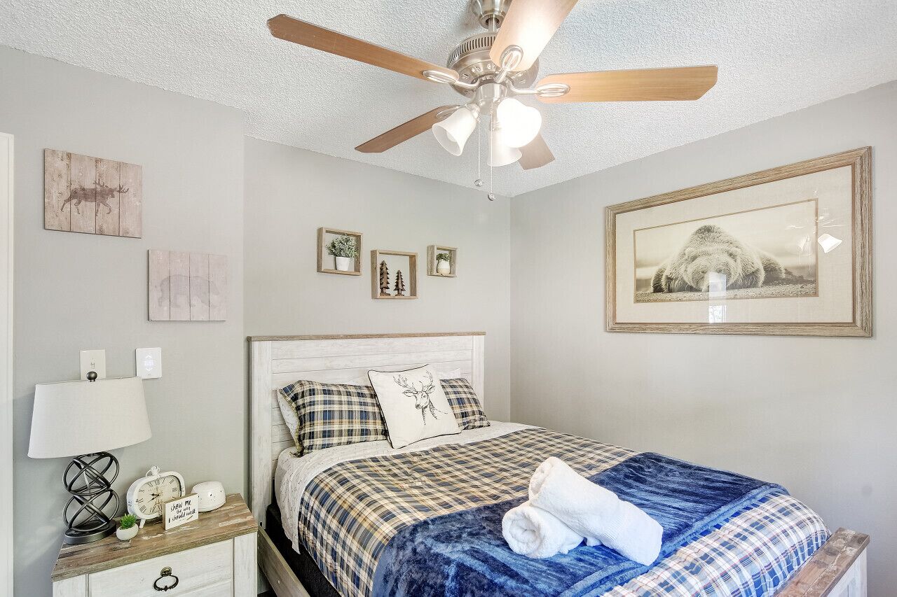 A bedroom with a bed, a nightstand, a ceiling fan, and wall art.