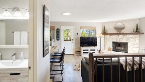 A modern living room with a fireplace, a television, and a dining area with chairs and a table. - The Tree House - Cozy, mountain cabin (Evergreen)