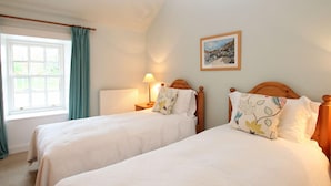 A bedroom with two single beds, a window with curtains, a bedside table with a lamp, and a framed picture on the wall. - The Colonsay Hotel (Isle of Colonsay)