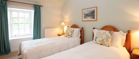 Un dormitorio con dos camas individuales, una ventana con cortinas, una mesita de noche con lámpara y un cuadro en la pared.