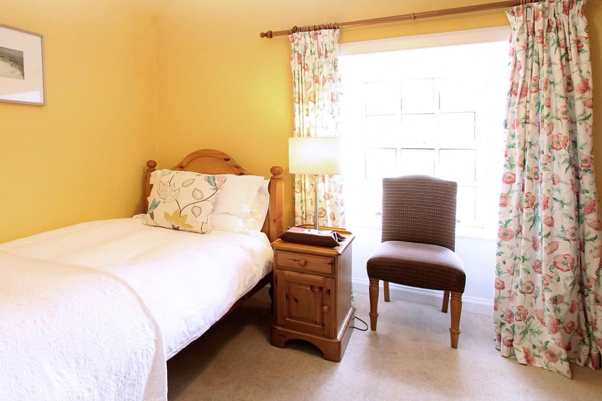 A bedroom with a bed, nightstand, chair, and a window with floral curtains.