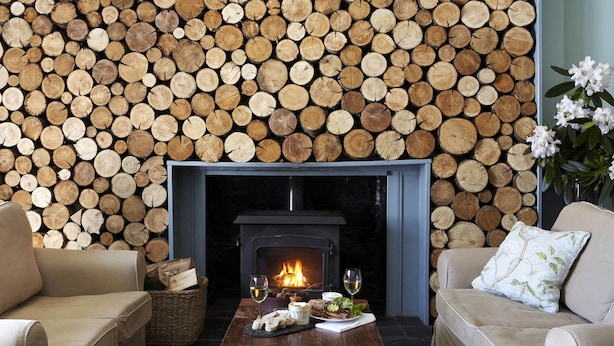 A cozy living room with a fireplace, a sofa, a coffee table with food and drink, and a log wall. - The Colonsay Hotel (Isle of Colonsay)