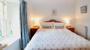 A neatly made bed with a patterned bedspread, two bedside lamps, and a window with curtains. - The Colonsay Hotel (Isle of Colonsay)