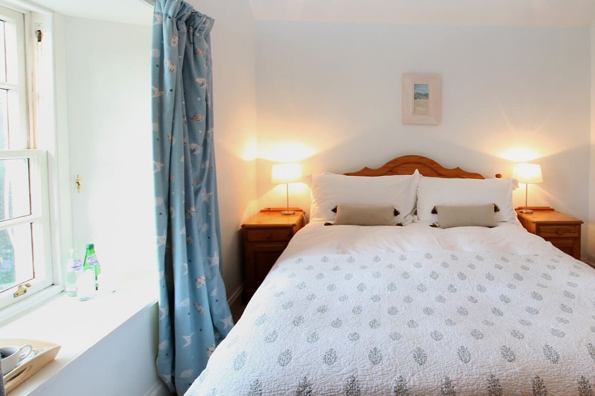 A neatly made bed with a patterned bedspread, two bedside lamps, and a window with curtains.