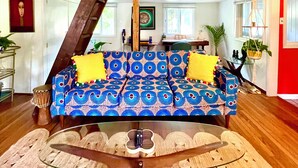 A spacious living room with a high ceiling, a wooden staircase, a blue patterned sofa, and a glass coffee table.