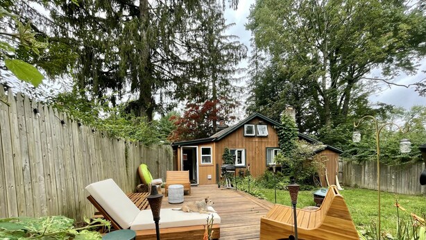 A wooden deck with a lounge chair and a table, a small wooden house with a door and windows, and a wooden fence.