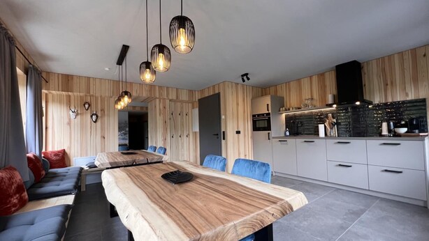 A modern kitchen with a wooden countertop, a dining area with a long table and blue chairs, and pendant lighting. - Bergquell Willingen App. 4 (Willingen)