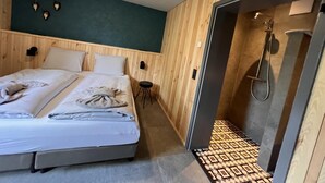 A hotel room with a bed, a small stool, a wall-mounted light, and a shower area. - Bergquell Willingen App. 4 (Willingen)