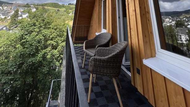 A wooden balcony with wicker chairs and a view of a town and greenery. - Bergquell Willingen App. 6 (Willingen)