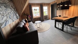 A modern living room with a wooden accent wall, a leather sofa, a round coffee table, and a dining area with a wooden table and chairs. - Bergquell Willingen App. 6 (Willingen)