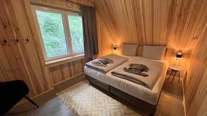 A wooden-paneled room with a bed, two bedside lamps, a small table, and a window with curtains. - Bergquell Willingen App. 6 (Willingen)
