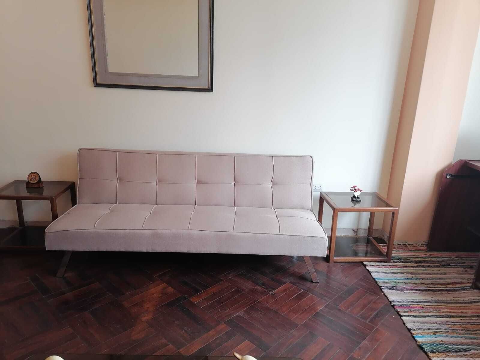 A room with a sofa, two small side tables, a wooden floor, and a patterned rug.
